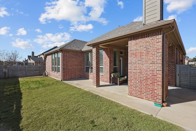 back of property with a patio, a yard, a fenced backyard, a chimney, and brick siding