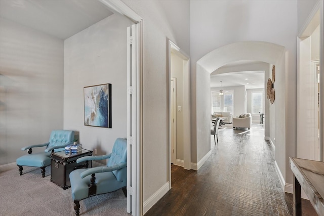 hallway with arched walkways, baseboards, and wood finished floors