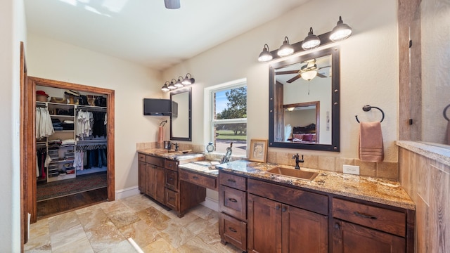 bathroom featuring ceiling fan, a spacious closet, two vanities, and a sink