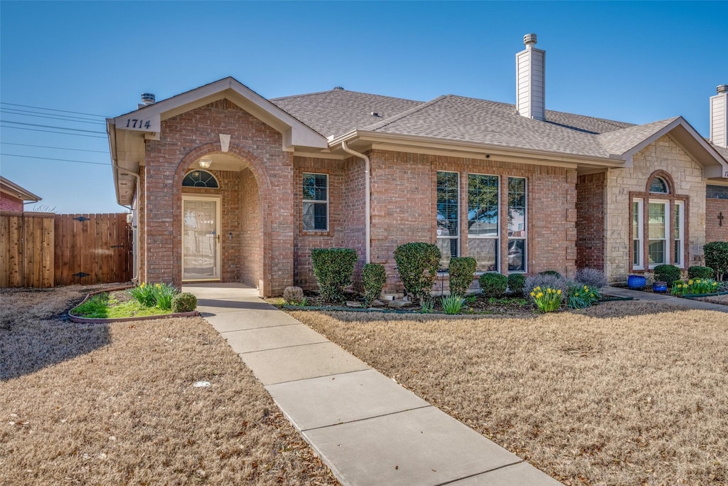 ranch-style house featuring brick siding, roof with shingles, a chimney, and fence