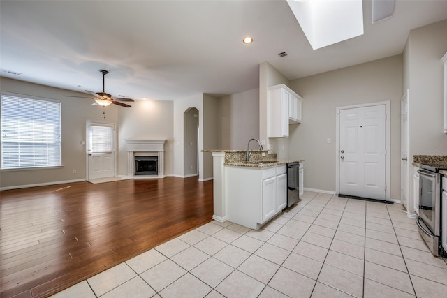 kitchen with stainless steel range with electric stovetop, a fireplace with raised hearth, black dishwasher, white cabinetry, and light stone countertops