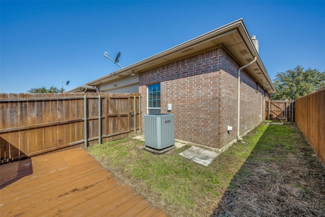 exterior space with central air condition unit, a deck, a fenced backyard, a yard, and brick siding