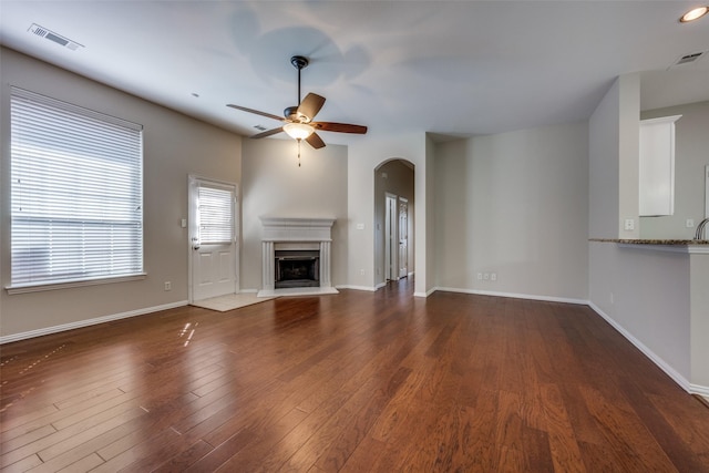 unfurnished living room with wood finished floors, baseboards, a ceiling fan, visible vents, and a fireplace with raised hearth