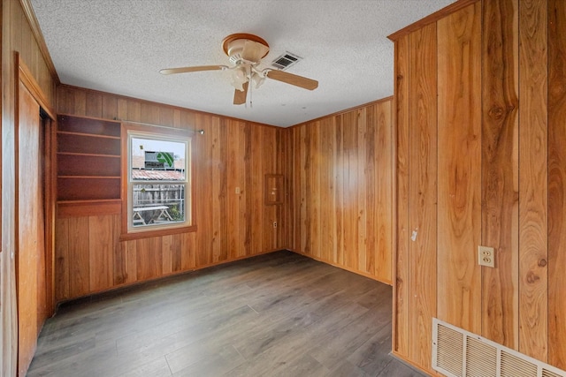 empty room with wooden walls, wood finished floors, visible vents, and a textured ceiling