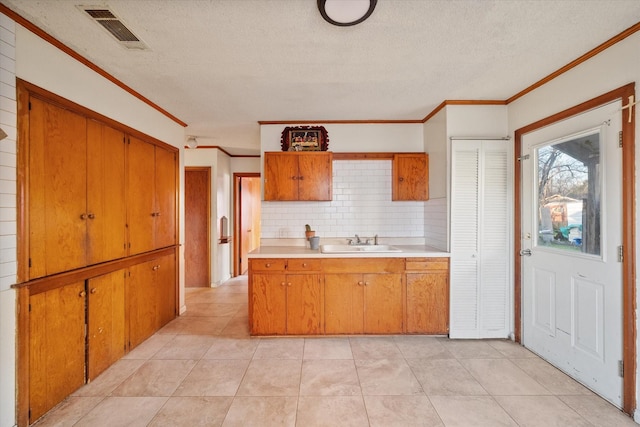 kitchen featuring visible vents, brown cabinets, a sink, light countertops, and decorative backsplash