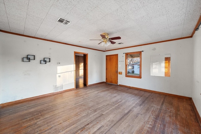 empty room with a ceiling fan, visible vents, wood finished floors, baseboards, and crown molding