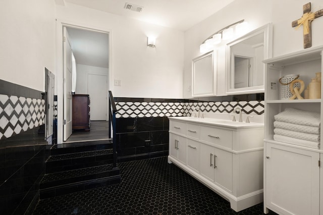 bathroom featuring visible vents, a sink, tile walls, wainscoting, and double vanity