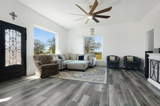 living area with a glass covered fireplace, ceiling fan, and wood finished floors