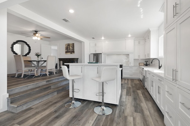 kitchen with visible vents, a kitchen island, decorative backsplash, freestanding refrigerator, and white cabinets