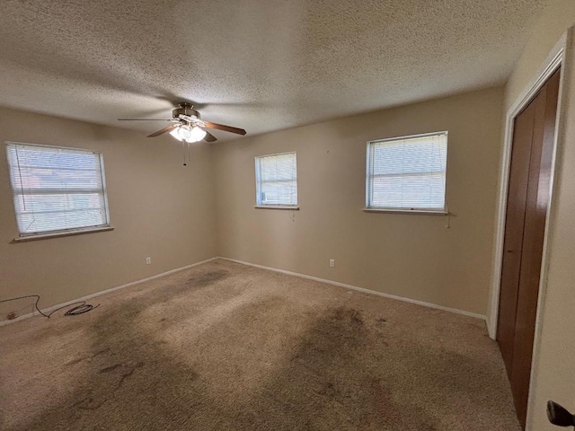 unfurnished bedroom featuring a ceiling fan, a textured ceiling, a closet, carpet flooring, and baseboards