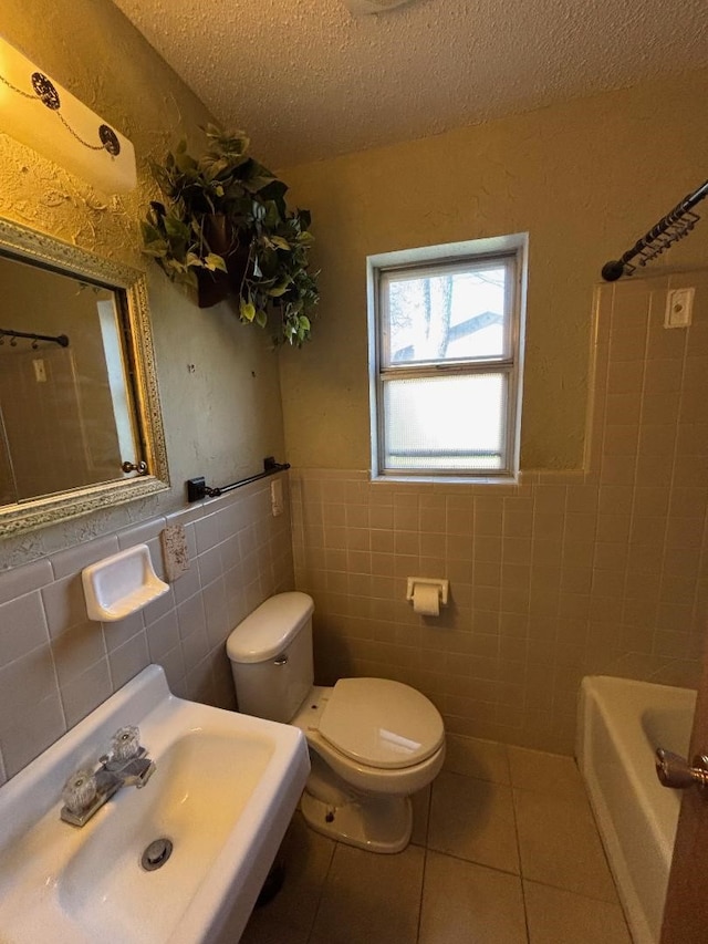 full bathroom with tile patterned flooring, toilet, a bathing tub, a textured ceiling, and a sink