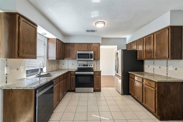 kitchen featuring visible vents, a sink, stainless steel appliances, decorative backsplash, and light stone countertops