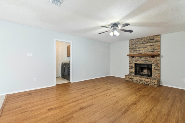 unfurnished living room with visible vents, a ceiling fan, a textured ceiling, light wood finished floors, and a brick fireplace