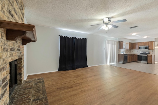 unfurnished living room with visible vents, a brick fireplace, ceiling fan, baseboards, and light wood-style floors