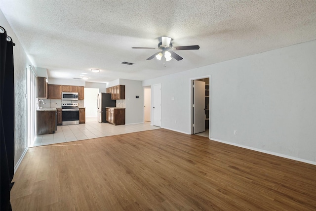 unfurnished living room featuring visible vents, a ceiling fan, a sink, a textured ceiling, and light wood-style floors