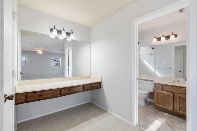 full bath featuring baseboards, ceiling fan, toilet, vanity, and a textured ceiling