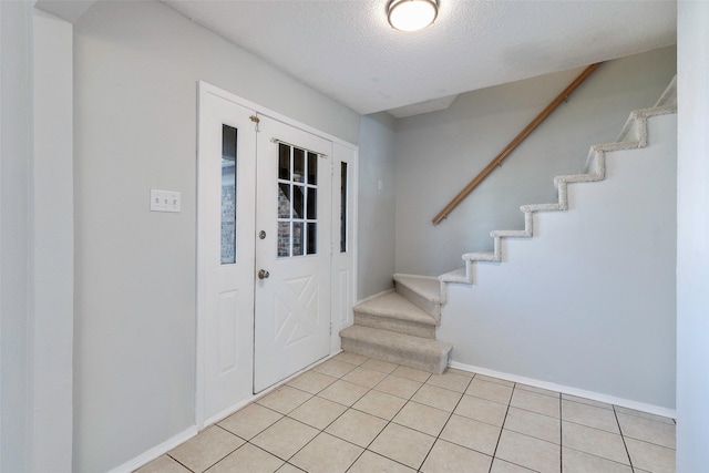 foyer entrance with stairway, light tile patterned floors, baseboards, and a textured ceiling