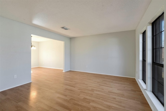 spare room with baseboards, visible vents, light wood finished floors, and a textured ceiling