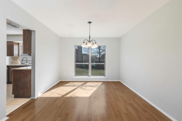 unfurnished dining area featuring a chandelier, light wood-style flooring, and baseboards