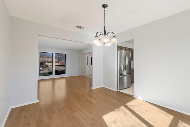 unfurnished dining area with light wood-type flooring, baseboards, a notable chandelier, and visible vents