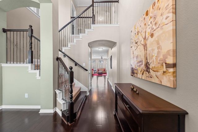 interior space with dark wood finished floors, a high ceiling, baseboards, and arched walkways