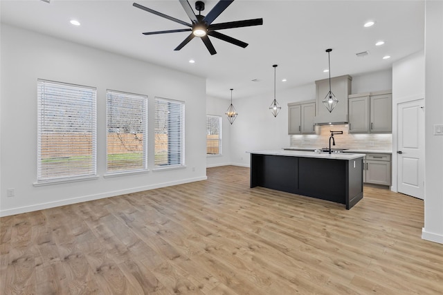 kitchen with a sink, decorative backsplash, light countertops, gray cabinetry, and ceiling fan with notable chandelier