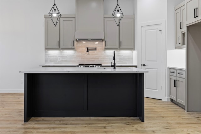 kitchen featuring light wood-style floors, a center island with sink, backsplash, and a sink