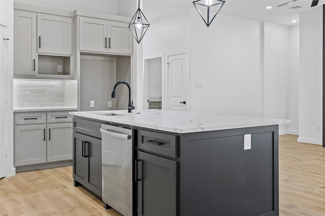 kitchen with light wood-style flooring, a kitchen island with sink, gray cabinets, a sink, and tasteful backsplash