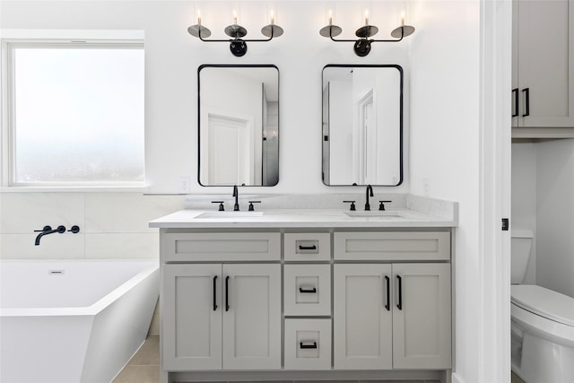 bathroom featuring a soaking tub, a sink, toilet, and double vanity