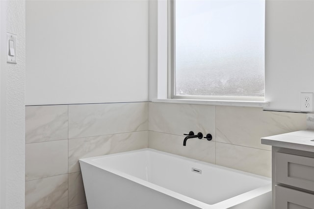 bathroom with tile walls, a bath, and vanity