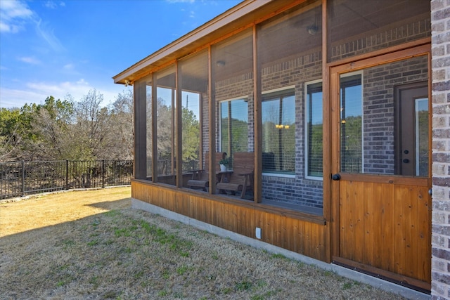 view of side of home featuring fence, brick siding, and a sunroom