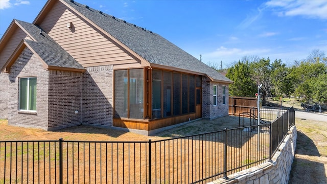 view of side of home with brick siding, a fenced backyard, roof with shingles, and a sunroom