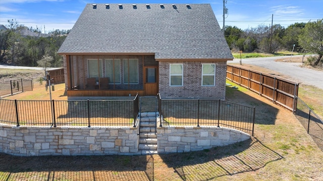 rear view of property featuring brick siding, fence private yard, and roof with shingles