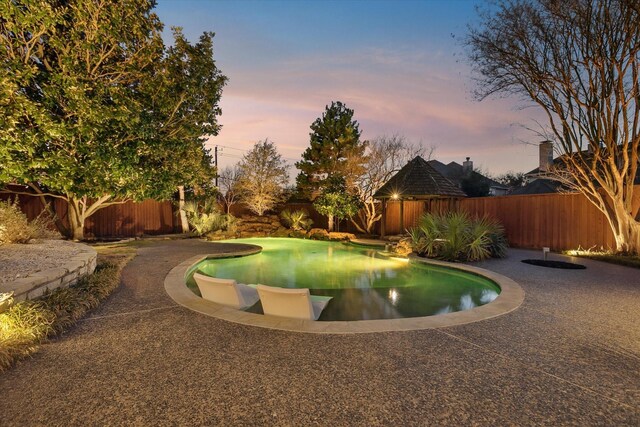 pool at dusk featuring a patio area and a fenced backyard