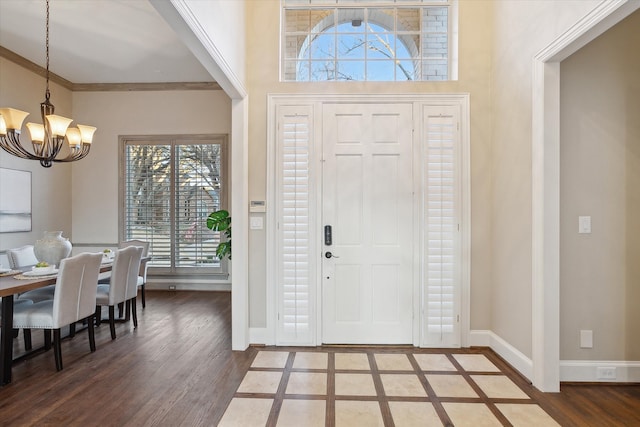 foyer featuring wood finished floors, baseboards, an inviting chandelier, ornamental molding, and a towering ceiling