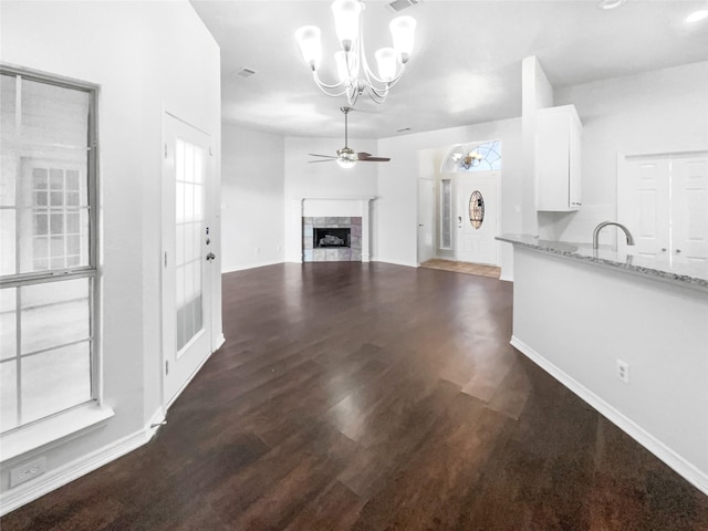 unfurnished living room featuring dark wood-style floors, visible vents, baseboards, a tiled fireplace, and ceiling fan with notable chandelier