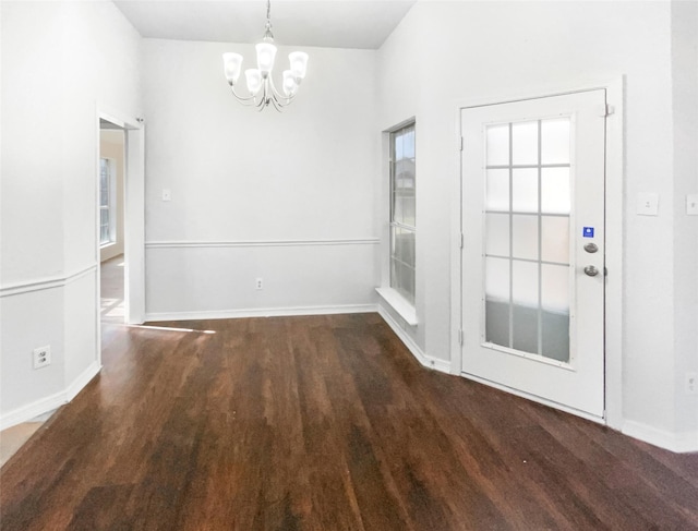 unfurnished dining area with a wealth of natural light, an inviting chandelier, baseboards, and wood finished floors