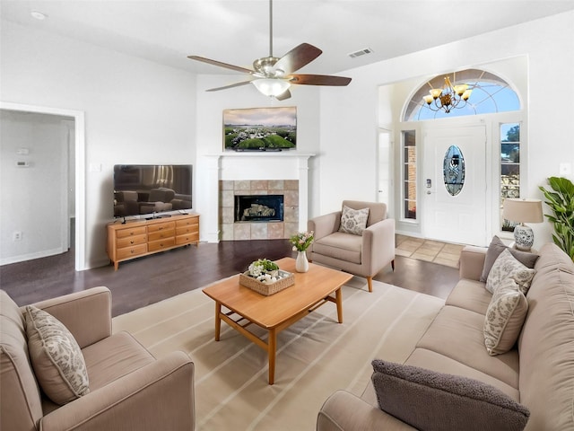 living room with visible vents, ceiling fan with notable chandelier, wood finished floors, and a tile fireplace