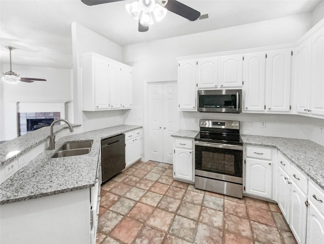 kitchen with light stone countertops, a sink, a tile fireplace, stainless steel appliances, and white cabinetry