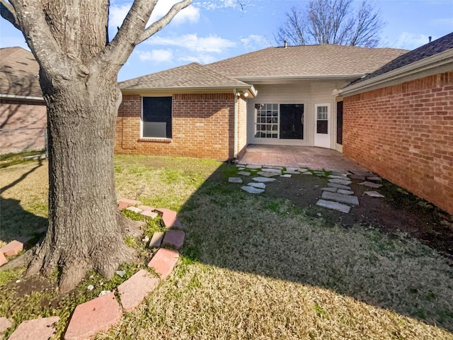 rear view of house featuring a yard, a patio area, brick siding, and roof with shingles