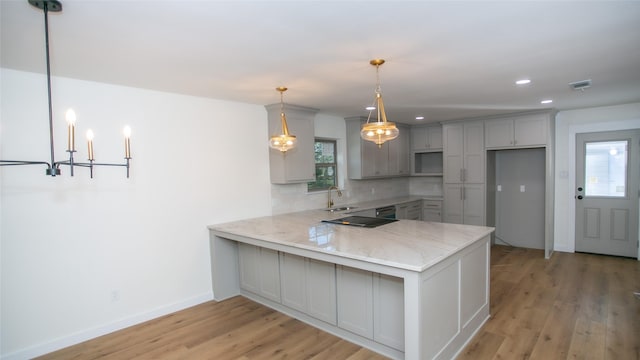 kitchen featuring light stone countertops, a peninsula, gray cabinets, light wood-style floors, and backsplash