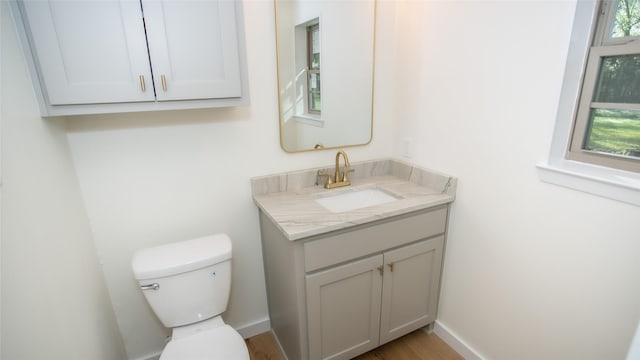 bathroom with baseboards, toilet, a healthy amount of sunlight, and vanity