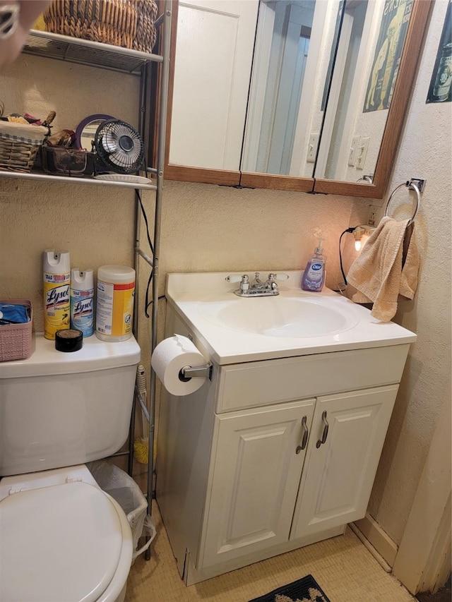 half bath with vanity, toilet, and a textured wall