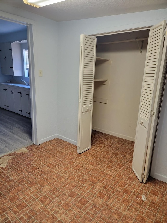 unfurnished bedroom featuring a closet, brick floor, and baseboards