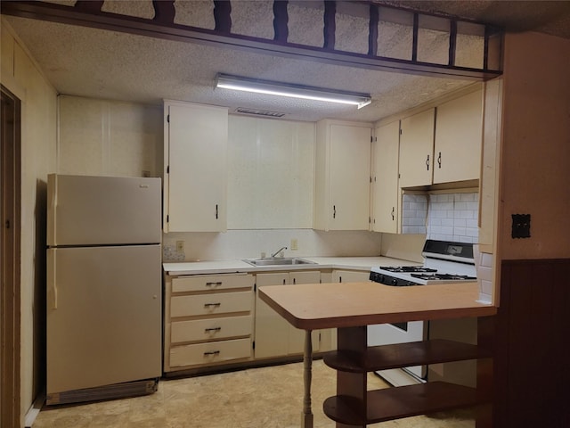 kitchen featuring light countertops, gas range oven, freestanding refrigerator, a textured ceiling, and a sink