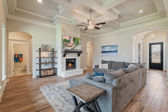 living area featuring ceiling fan, arched walkways, a stone fireplace, visible vents, and wood finished floors