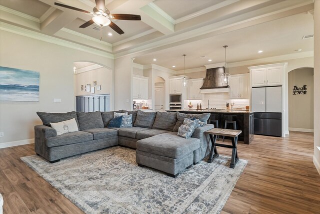 living room with baseboards, arched walkways, ornamental molding, ceiling fan, and light wood finished floors
