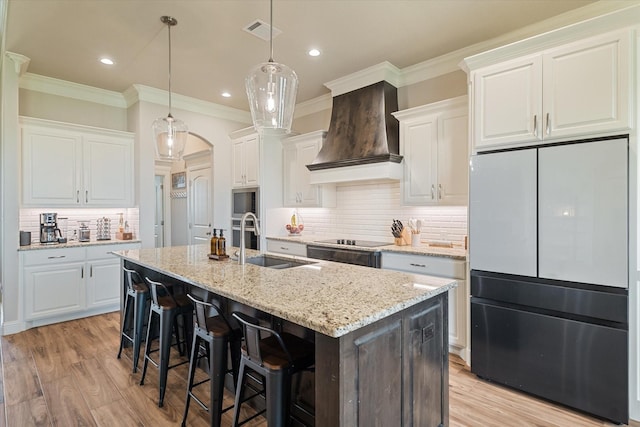 kitchen with custom exhaust hood, an island with sink, visible vents, fridge, and a sink