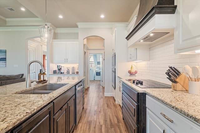 kitchen with arched walkways, white cabinetry, appliances with stainless steel finishes, a sink, and custom range hood