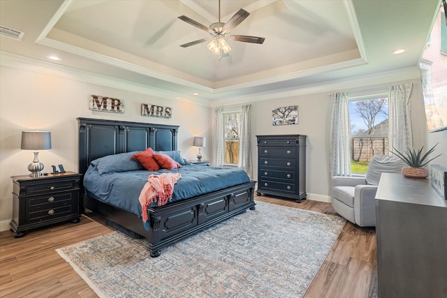 bedroom with a tray ceiling, light wood finished floors, baseboards, and visible vents